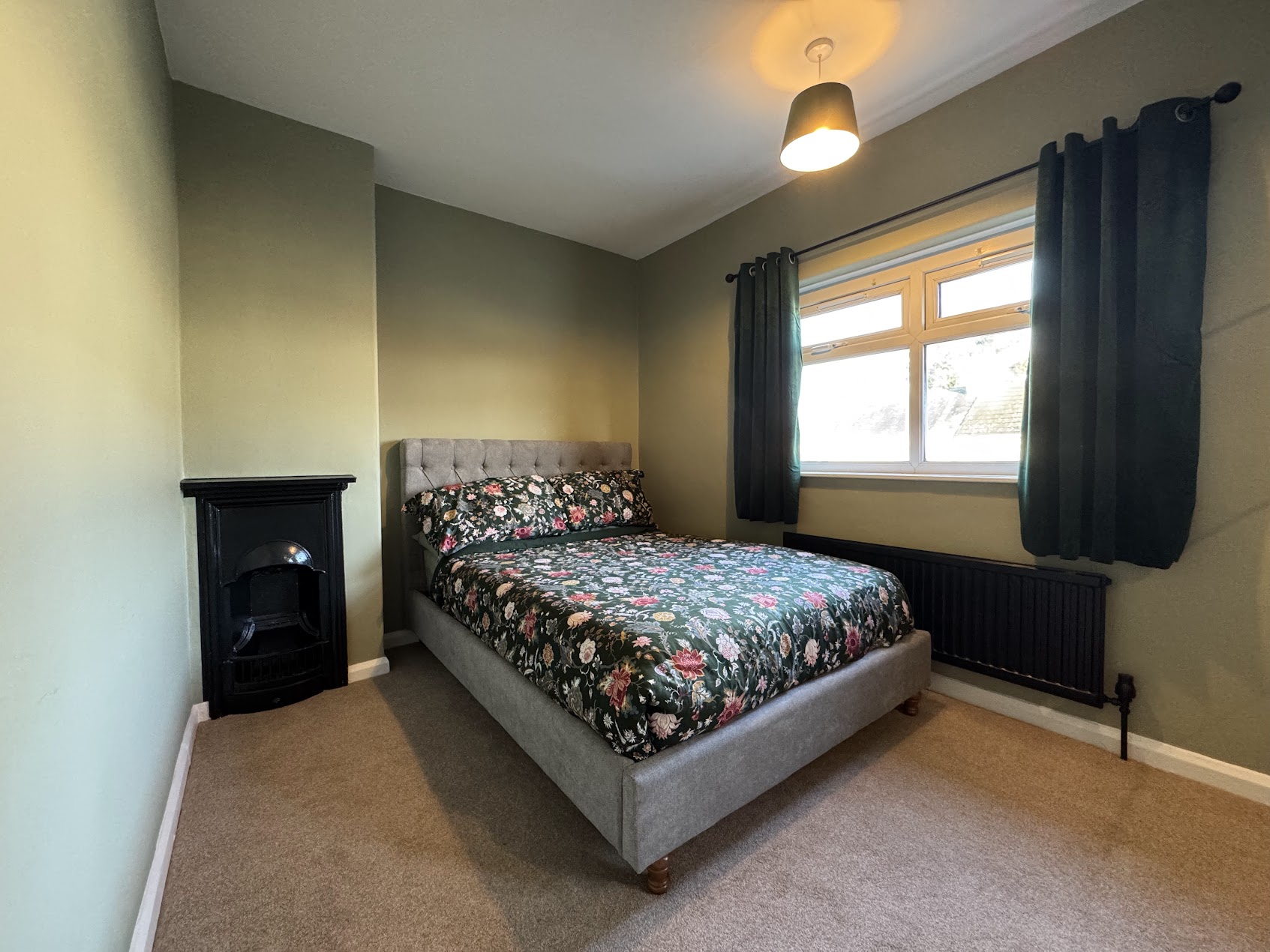 Redecorated Leeds bedroom with olive-green walls, a black fireplace and floral bedding