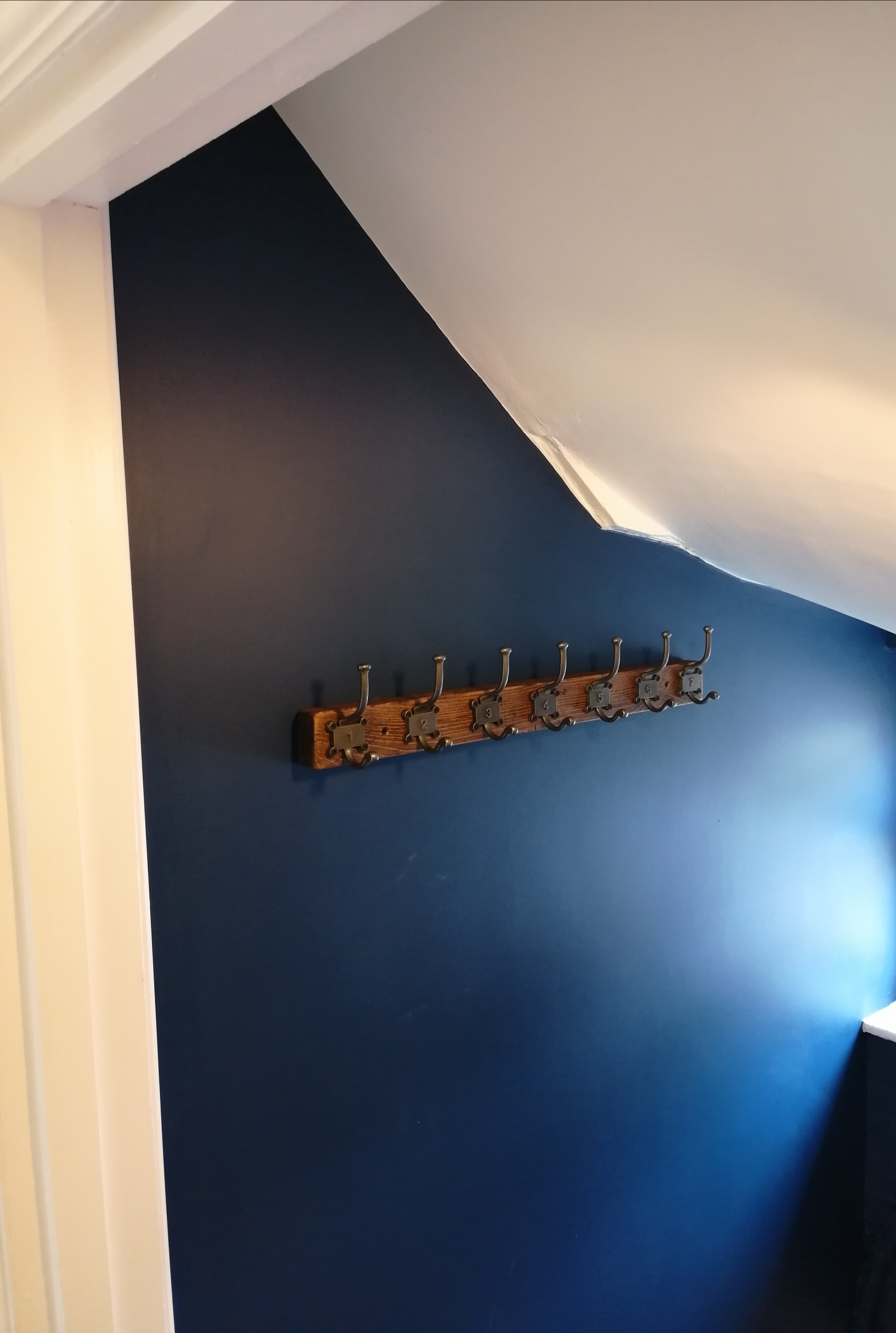 Freshly painted navy wall beneath a staircase with a wooden coat rack